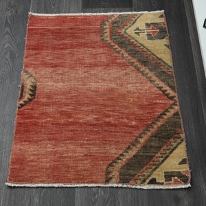 Puede incluir: Una alfombra roja, marrón y beige con estampado y borde con flecos. La alfombra tiene un diseño geométrico con flechas y otras formas.