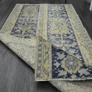 Puede incluir: Una alfombra de color azul y beige con flecos. La alfombra está doblada por la mitad y se puede ver el revés.