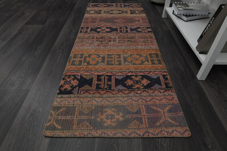 May include: A long, narrow rug with a colourful, geometric pattern. The rug has a dark background with shades of red, orange, and blue. The pattern is made up of repeating shapes and lines.