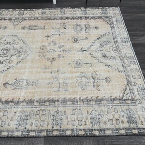 May include: A rectangular area rug featuring a light beige base with intricate patterns in shades of charcoal grey and muted brown. The design includes a central medallion surrounded by symmetrical floral and geometric motifs with a wide border.
