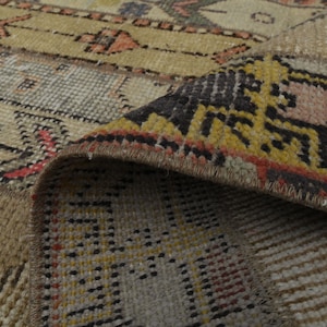 May include: Close-up of a woven rug with a geometric pattern in shades of brown, beige, yellow, red, and black. The rug has a fringe border.