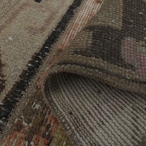 May include: Close-up of a woven rug with a brown, beige, and pink geometric pattern. The rug is folded over, showing the underside of the weave.