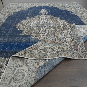 May include: A vintage rug with a blue center and a cream-colored border. The rug has a floral pattern and is folded in half.