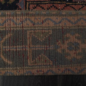 May include: Close-up of the bottom edge of a rug with a geometric pattern in shades of brown, red, and blue.