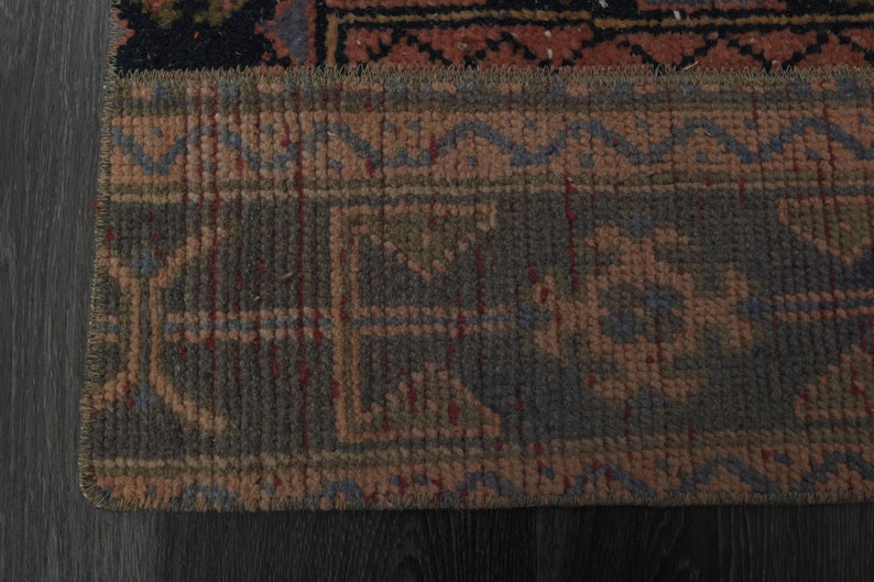 May include: Close-up of the bottom edge of a rug with a geometric pattern in shades of brown, red, and blue.
