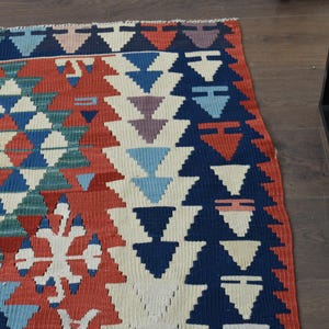 K&ouml;nnte beinhalten: Ein bunter Teppich mit einem geometrischen Muster in Rot-, Blau-, Gr&uuml;n- und Wei&szlig;t&ouml;nen. Der Teppich hat ein traditionelles Design mit sich wiederholenden Dreiecken und Rauten.