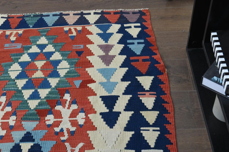 K&ouml;nnte beinhalten: Ein bunter Teppich mit einem geometrischen Muster in Rot-, Blau-, Gr&uuml;n- und Wei&szlig;t&ouml;nen. Der Teppich hat ein traditionelles Design mit sich wiederholenden Dreiecken und Rauten.