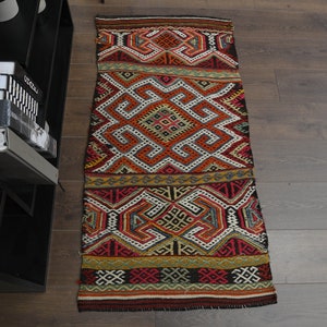 Puede incluir: Una alfombra larga y estrecha con un patrón geométrico en tonos de rojo, naranja, amarillo, azul y negro. La alfombra tiene un aspecto tradicional, tejido a mano.