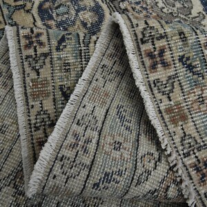May include: Close-up of the fringe on a beige and blue patterned rug. The fringe is white and the rug has a woven texture.