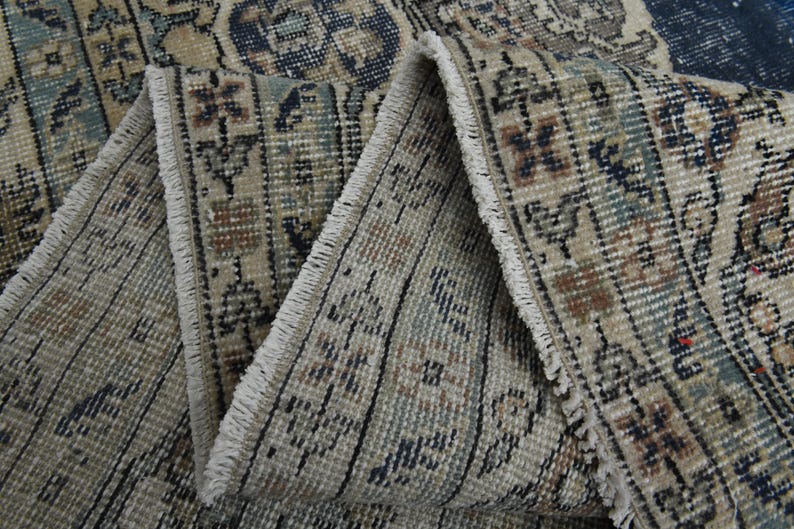 May include: Close-up of the fringe on a beige and blue patterned rug. The fringe is white and the rug has a woven texture.