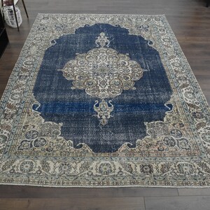 May include: A vintage rug with a blue center and a cream-colored border. The rug has a floral pattern and a distressed look.