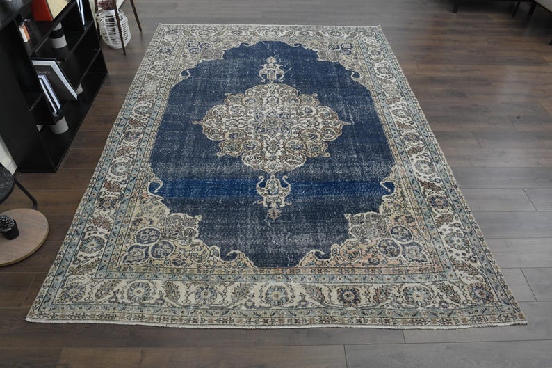 May include: A vintage rug with a blue center and a cream-colored border. The rug has a floral pattern and a distressed look.