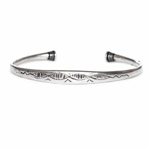 May include: A silver-toned cuff bracelet with an open design. The bracelet features etched geometric patterns along the front and textured ends. The jewelry is displayed against a white background.