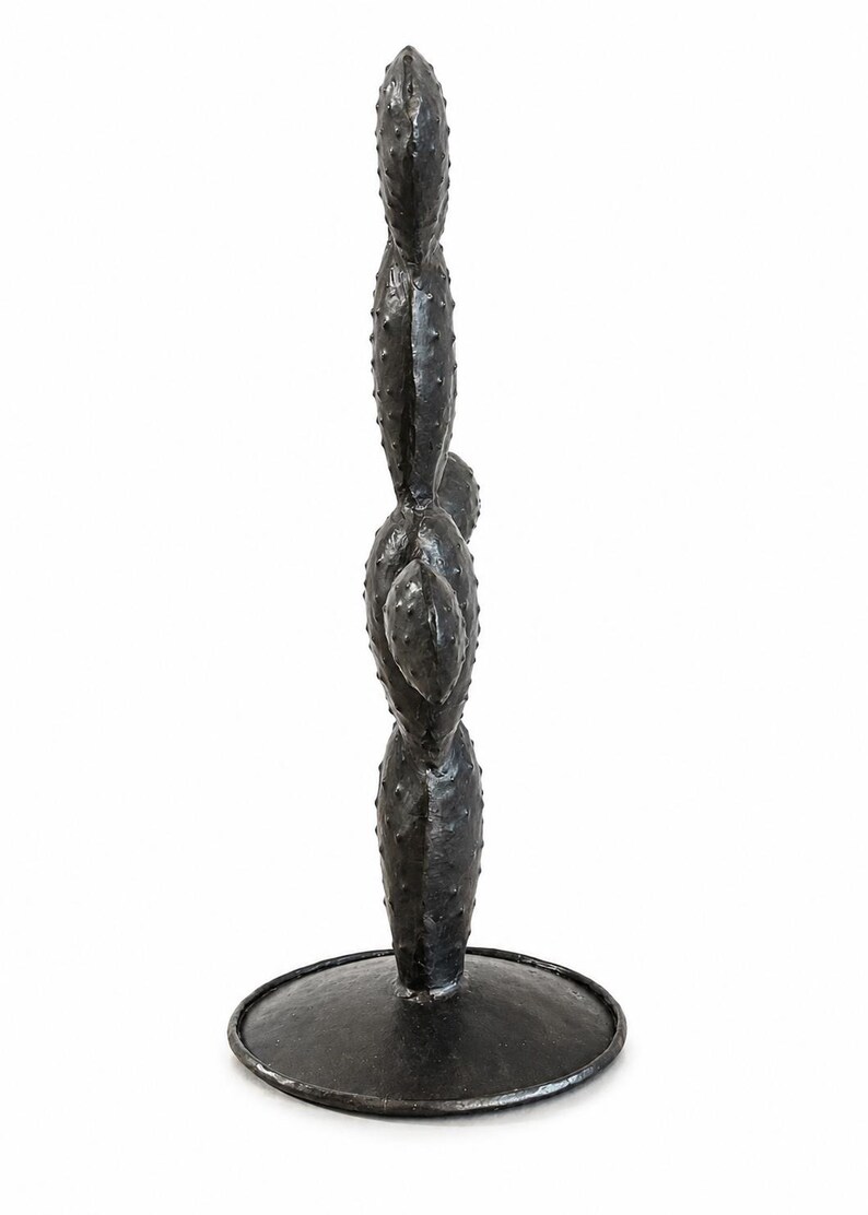 May include: A dark charcoal gray metal sculpture shaped like a prickly pear cactus with multiple stacked, oval-shaped pads featuring small raised bumps across the surface. The cactus stands upright on a circular, flat metal base of the same color.