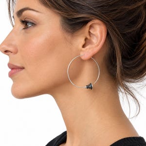 May include: A large, thin silver hoop earring featuring a small, conical black and silver striped bead accent at the bottom closure. The earring is circular in shape and has a minimalist wire construction that loops through the earlobe.