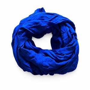 Può includere: Una sciarpa ad anello di colore blu reale vibrante, caratterizzata da un design a ciclo continuo con una consistenza del tessuto morbida, leggera e leggermente stropicciata. La sciarpa è disposta in forma circolare, mostrando il colore.