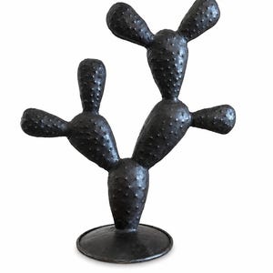 May include: A dark charcoal-colored cactus sculpture featuring a textured, bumpy surface with multiple rounded pads extending from a central base. The object stands upright on a circular, flat pedestal, showcasing a uniform matte finish throughout.