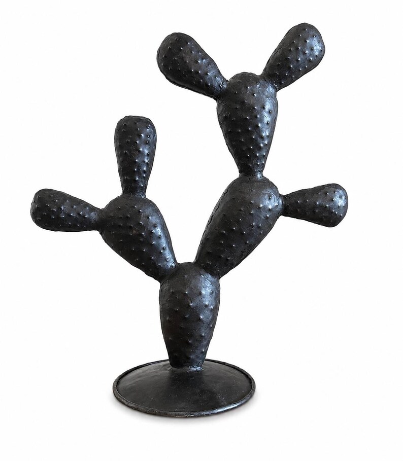 May include: A dark charcoal-colored cactus sculpture featuring a textured, bumpy surface with multiple rounded pads extending from a central base. The object stands upright on a circular, flat pedestal, showcasing a uniform matte finish throughout.