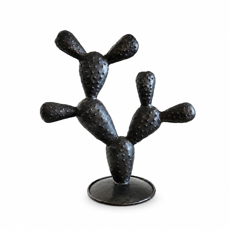May include: A black, textured cactus sculpture featuring multiple rounded, paddle-shaped segments with small, raised bumps across the surface. The cactus is mounted on a circular, flat base, creating a stable, upright, and decorative object.