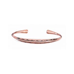 Può includere: Un bracciale rigido in metallo color rame dal design aperto. La superficie del bracciale presenta un rilievo centrale orizzontale decorato con una serie di piccole rientranze triangolari scure lungo il bordo superiore, creando un motivo.