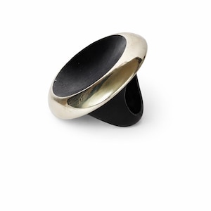 Peut inclure: Une bague moderne avec une bande argentée entourant un centre ovale noir. La bague a une bande épaisse et arrondie et un design épuré et minimaliste, parfait pour un usage quotidien.