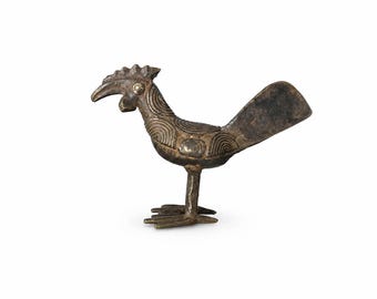 May include: A bronze-toned metal figurine of a bird with a prominent crest, a curved beak, and a fan-shaped tail. The body features engraved concentric circular patterns and smooth circular accents on the neck and side, standing on two legs.