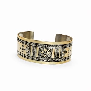 Peut inclure: Un bracelet manchette argenté et doré avec un design ouvert. Le bracelet présente des motifs géométriques noirs gravés complexes. Le bracelet est une large bande avec une finition polie, adaptée au quotidien.