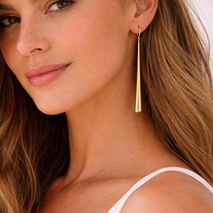 Peut inclure: Longues boucles d'oreilles dorées effilées. Les boucles d'oreilles sont suspendues à un petit crochet et pendent vers le bas, créant un look élégant. Un accessoire simple mais élégant.