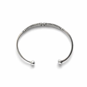 Könnte beinhalten: Ein silberfarbenes Armreif-Armband mit offenem Design. Das Armband hat einen dekorativen Mittelteil mit geätzten Mustern und kleinen, abgerundeten Enden. Das Design ist schlicht und elegant, für den Alltag geeignet.