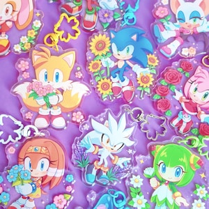 Könnte beinhalten: Eine Sammlung von durchsichtigen Acryl-Schlüsselanhängern mit verschiedenen Sonic the Hedgehog-Charakteren, darunter Sonic, Tails, Knuckles, Silver und Amy, die jeweils mit bunten Blumen illustriert und an sternförmigen oder runden Metallverschlüssen befestigt sind.