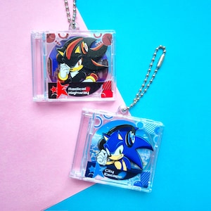 Puede incluir: Dos llaveros de plástico transparente con personajes de la serie de videojuegos Sonic the Hedgehog. El llavero de la izquierda presenta a Shadow the Hedgehog con el texto "Radical Highway". El llavero de la derecha presenta a Sonic the Hedgehog con el texto "City Escape".