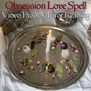 May include: A silver tray with a lit white candle, surrounded by crystals, leaves, and rosebuds. Two lit candles flank the tray, with bundles of herbs and text that reads "Obsession Love Spell Video Proof Tarot Reading".