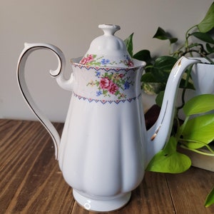 May include: White porcelain teapot with a floral pattern and gold trim. The teapot has a lid and a handle.