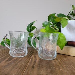 Puede incluir: Dos tazas de vidrio transparente con un dise&ntilde;o floral. Las tazas tienen una textura acanalada y est&aacute;n sobre una superficie de madera.