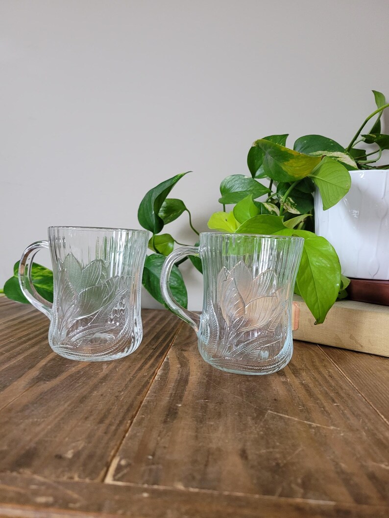 Puede incluir: Dos tazas de vidrio transparente con un dise&ntilde;o floral. Las tazas tienen una textura acanalada y est&aacute;n sobre una superficie de madera.