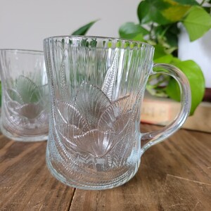 Puede incluir: Dos tazas de vidrio transparente con un dise&ntilde;o floral. Las tazas tienen un asa y est&aacute;n hechas de vidrio grueso.