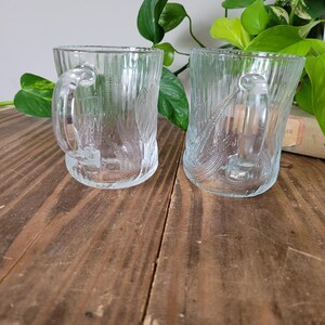 Puede incluir: Dos tazas de vidrio transparente con un dise&ntilde;o texturizado. Las tazas tienen asas y est&aacute;n sobre una superficie de madera.