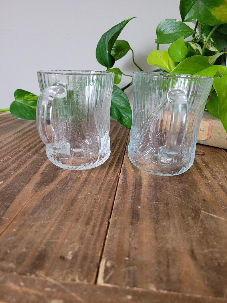 Puede incluir: Dos tazas de vidrio transparente con un dise&ntilde;o texturizado. Las tazas tienen asas y est&aacute;n sobre una superficie de madera.