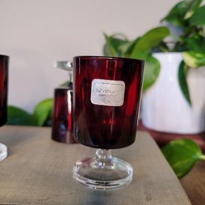 Puede incluir: Un juego de tres vasos de chupito de vidrio rojo con base de vidrio transparente. Los vasos tienen una etiqueta plateada que dice "Krinner" y "Hand Made".