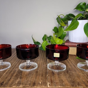 Könnte beinhalten: Vier klare Glasschalen mit roten Glasschalen und klaren Glasstielen. Die Schalen stehen auf einer Holzoberfläche.