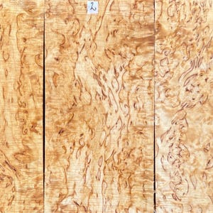 Può includere: Tre tavole di legno rettangolari caratterizzate da un colore di base marrone chiaro con intricati motivi a venature scure e vorticose. La tavola centrale è contrassegnata dal numero 2 in un piccolo quadrato bianco sul bordo superiore, con venature naturali.