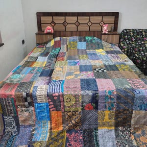 May include: A rectangular patchwork quilt featuring a variety of fabric squares in diverse colors, patterns, and textures. The quilt is stitched with visible running thread lines throughout, creating a quilted surface that covers the entire bed.