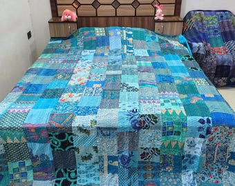 Op de afbeelding: Een patchwork sprei bestaande uit diverse blauwe, turquoise en petrolkleurige stoffen vierkanten met verschillende bloem-, geometrische en paisley-patronen. De sprei is voorzien van zichtbare stiklijnen en ligt over een bed met een houten hoofdbord.