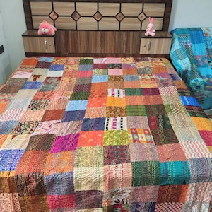 May include: A patchwork quilt featuring a grid of multicolored fabric squares with various patterns and textures. The quilt is spread over a bed with a dark brown wooden headboard that includes integrated side storage compartments and small plush toys.