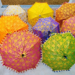 以下が含まれることがあります： 鮮やかな色の開いた傘のコレクション。複雑な花柄模様が特徴です。傘は黄色、オレンジ、紫、緑、ピンクの色合いで、装飾的なトリムが付いています。傘は円形に配置されています。