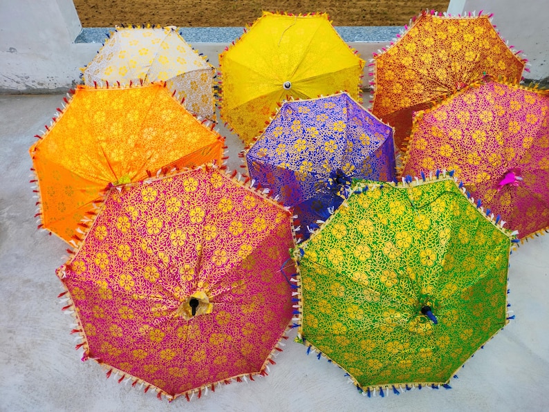以下が含まれることがあります： 鮮やかな色の開いた傘のコレクション。複雑な花柄模様が特徴です。傘は黄色、オレンジ、紫、緑、ピンクの色合いで、装飾的なトリムが付いています。傘は円形に配置されています。