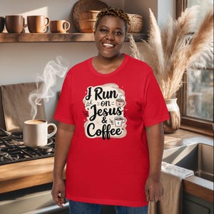 Puede incluir: Una camiseta roja con el texto "I Run on Jesus & Coffee" en un diseño decorativo. La camiseta presenta una taza de café y un símbolo de cruz. La persona de la imagen está sonriendo.