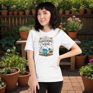 May include: White t-shirt featuring the text "Powered by Gardening & Love" in a floral design. The graphic includes a blue watering can, potted plants, and the names "Liam" and "Noah". The shirt is worn by a person in a garden setting.