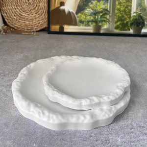 Puede incluir: Dos platos de cerámica blanca con un borde texturizado y ondulado. El plato más pequeño está apilado sobre el más grande.