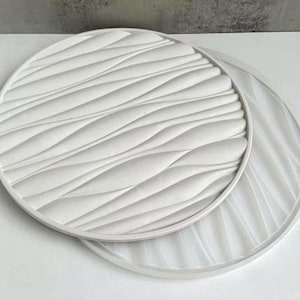 May include: Two white round silicone moulds with a wavy pattern. The mould on top has a more pronounced wave pattern than the mould on the bottom.